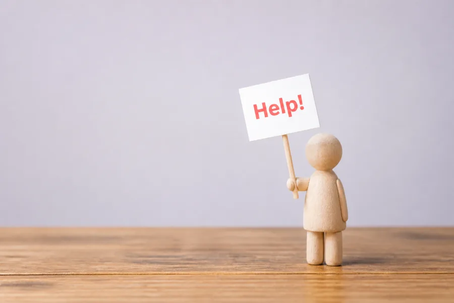 Puinen hahmo pitää Help-kylttiä vaalealla taustalla